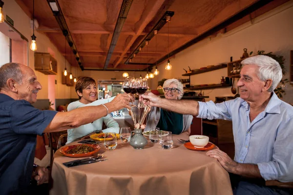 幸せな先輩の友人が夕食のためにレストランに座って 赤ワイングラスで乾杯します 屋内で一緒に食事を楽しむ成熟した人々 高齢者のライフスタイル 食べ物と飲み物 年金受給者の概念 — ストック写真