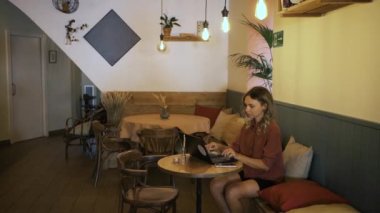 Kafkasyalı genç bir iş kadını bir kafede dizüstü bilgisayarla çalışırken, koruyucu yüz maskesi takan bir garson kahve fincanı getiriyor. Coronavirus salgını sırasında uzaktan kumanda..