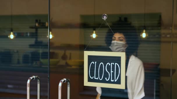 レストランの女性の所有者は 閉鎖隔離後に再オープン外科マスクを着用 アフリカ系アメリカ人のビジネス女性は コロナウイルスが発生した後 カメラを見て開いた看板を掛けます 新常態 — ストック動画