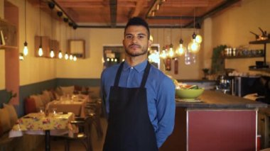 Kendine güveni tam, sakallı yakışıklı bir iş adamı göğsüne silah dayayıp modern bir restoranın yemek odasında duruyor. Afrikalı Amerikalı garson kararlılıkla kameraya bakıyor..