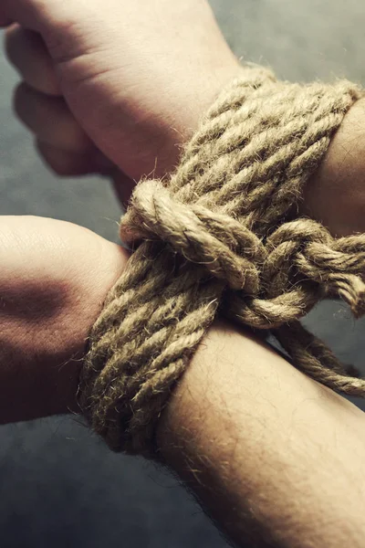 Male hands tied by a rough rope on a dark background close-up. Symbol of bondage, slavery