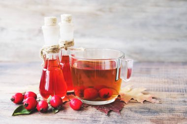 Alıç tentürü (dikenli elma, May-tree, whitethorn, hawberry) cam küçük şişe ve çay ahşap masada bir cam kupa içinde. Bitkisel ilaç.