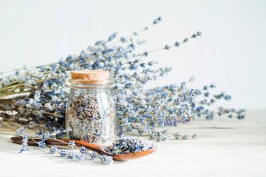 Cam şişe ve beyaz ahşap arka plan üzerinde lavanta ile kurutulmuş lavanta çiçekleri ve buket ile ahşap kaşık