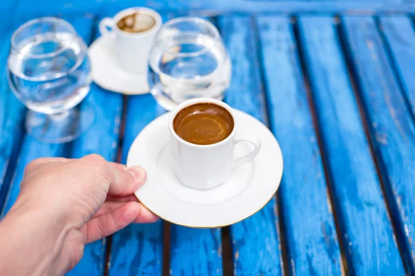Two cups of coffee and water glass on a blue wooden table.