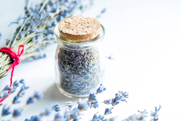 Glass bottle with dried lavender flowers and bouquet with lavender on white background, soft focus