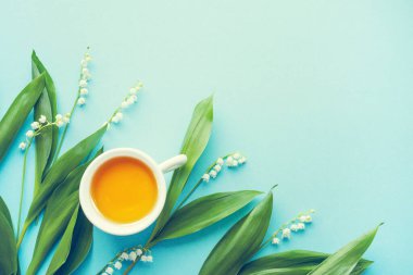 Bir fincan çay ve bir buket zambak mavi arka planda, üst manzara, kopyalama alanı