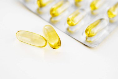 İki omega-3 kapsülü ve kapsülleri beyaz bir yüzeye yakın, yumuşak odaklı.