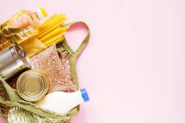 Yiyecek bağışları - yağ, karabuğday, makarna, süt, pembe arka planda bir market ızgarasında konserve yiyecekler, fotokopi alanının üst görüntüsü. Yiyecek teslimatı kavramı.