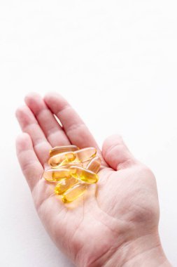 Bir kadının elinde iki omega-3 kapsülü, yumuşak odaklı, yakın plan.