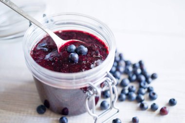 Beyaz ahşap bir yüzey üzerinde cam bir kavanozda taze yaban mersini ve yabanmersini reçeli. Yakın plan.