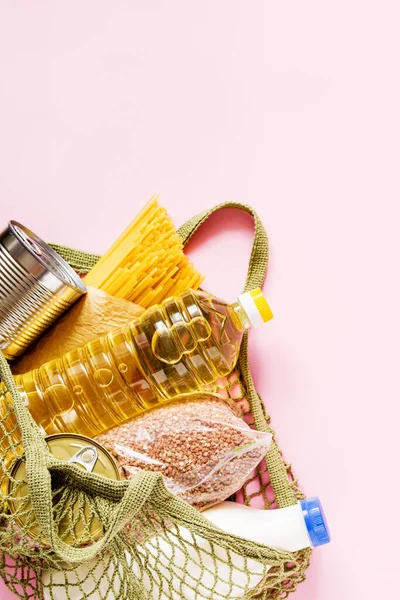 食品寄付 パスタ ピンクの背景に食料品グリッド内の缶詰食品 コピースペースのトップビュー 食品配送のコンセプト — ストック写真