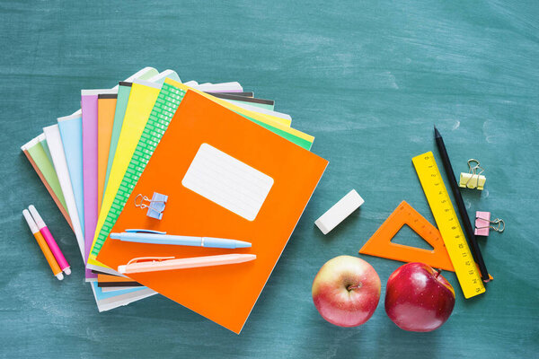 Back to school. Green blackboard with bright notebooks, pens, rulers, apples and scrapbook paper, top view