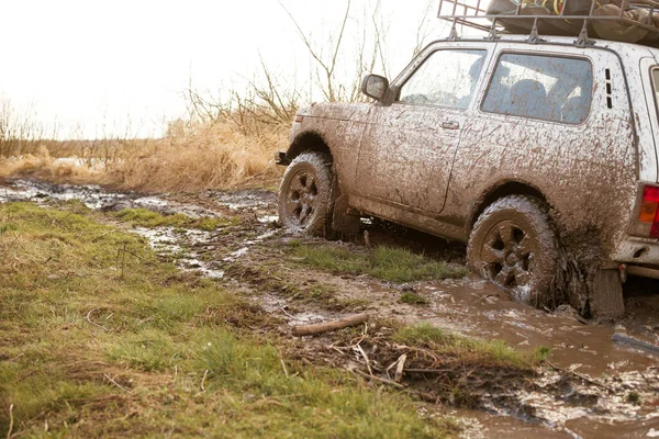 Dirty SUV is driving off-road with puddles and dirt close-up. Off-road travel