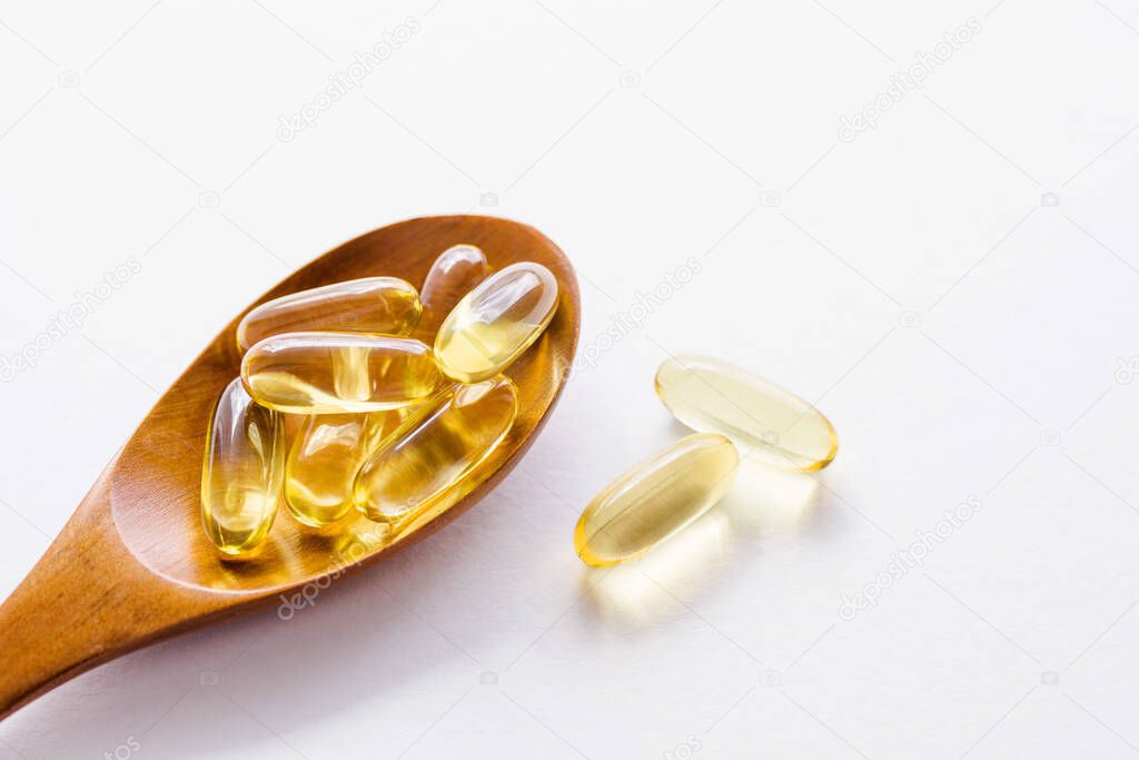 Fish fat oil capsules Omega-3 in wooden spoon on white background, close up