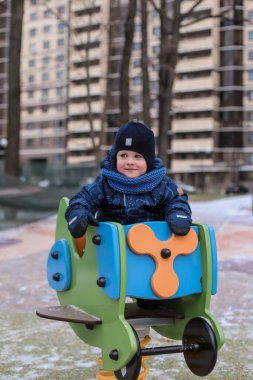 Şirin küçük çocuk kışın parkta yürüyor. Tulum, şapka ve eldiven giyiyor. Çocuk eğleniyor.