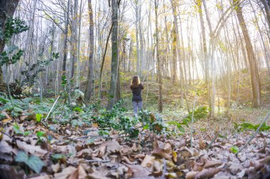 Genç kadın, günbatımında ormanda tek başına duran.