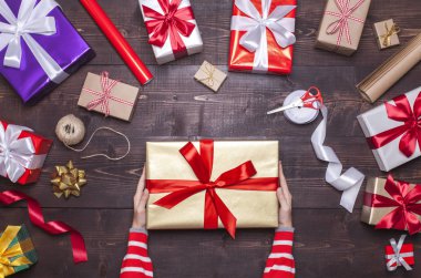 Mevcut holding kadın eller kutu çok renkli hediye ile ahşap arka plan üzerinde kırmızı yay ile kutuları düz stil yatıyordu.