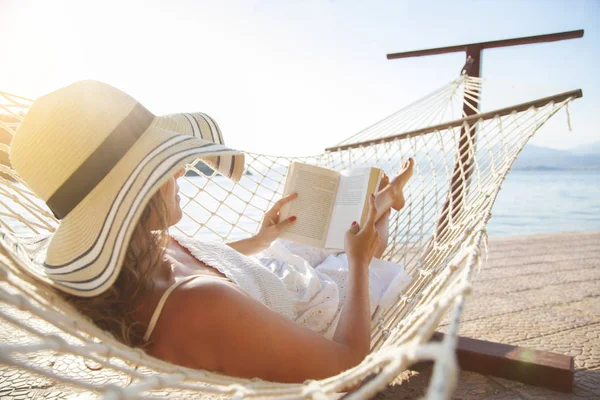 Ung kvinna, läser en bok i en hängmatta vid solnedgången. — Stockfoto