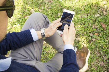 Genç adam akıllı telefonuyla parkta mesaj atıyor.