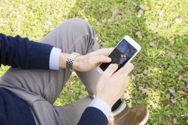 Genç adam akıllı telefonuyla parkta mesaj atıyor.