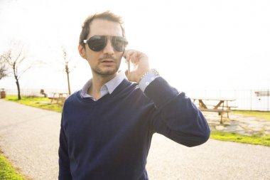 Genç adam parkta telefonla konuşuyor.