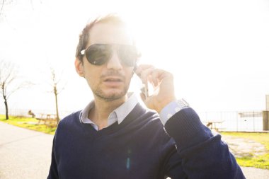 Genç adam parkta telefonla konuşuyor.