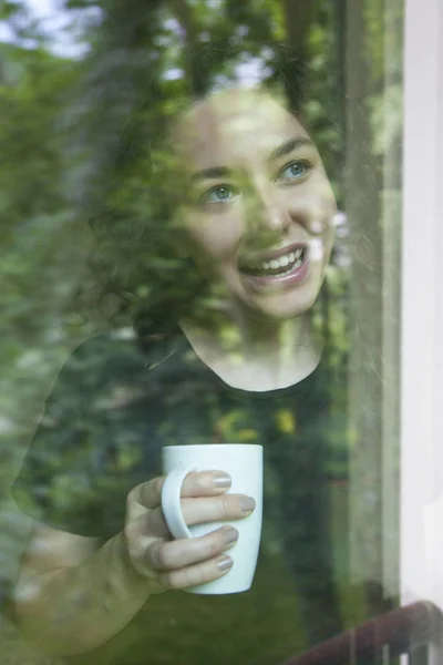 Молодая женщина смотрит из окна вид через стекло — стоковое фото