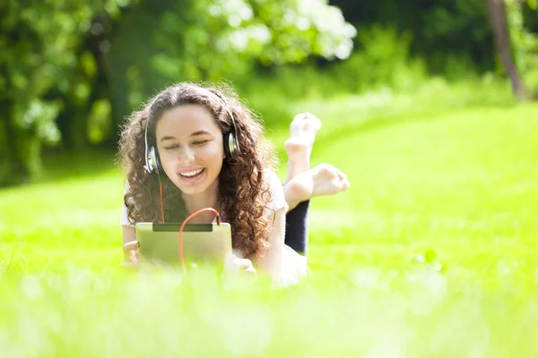 Mujer joven acostada en la hierba escuchando musi — Foto de Stock