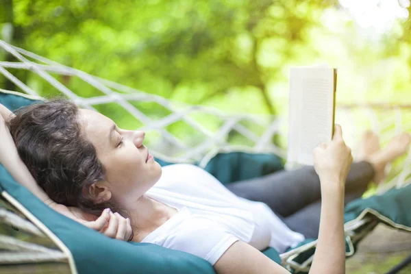 Mujer joven relajándose en hamaca con libro —  Fotos de Stock