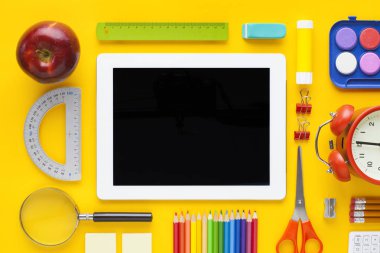 Sarı masada okul ve ofis malzemeleri ile boş tablet
