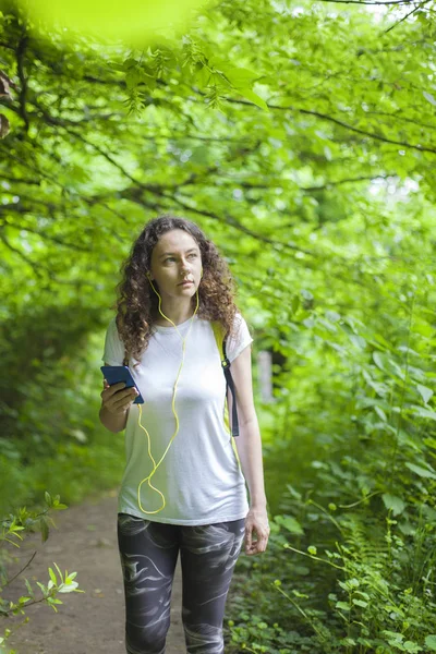 Mladá žena naslouchající hudbě při chůzi v lese — Stock fotografie
