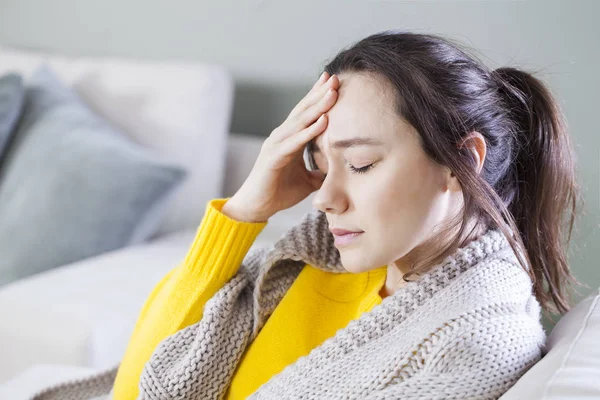 Mujer joven con dolor de cabeza sentada en el sofá — Foto de Stock