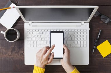 Ahşap ofis masasında akıllı telefon tutan kadın elleri.