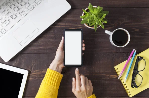 Woman hands holding smartphone at wooden office desktop, top vie — Stock Photo, Image