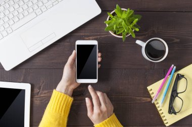 Ahşap ofis masasında akıllı telefon tutan kadın elleri.