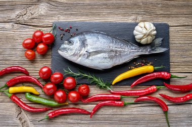 Ham dorada balık sebzeler eski ahşap arka plan üzerinde siyah arduvaz kesme tahtası üzerinde. Görünümü en çok, uzay kopyalayın. Sağlıklı gıda arka plan.