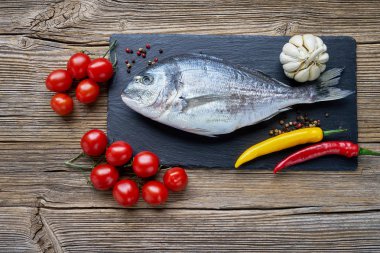 Ham dorada balık sebzeler eski ahşap arka plan üzerinde siyah arduvaz kesme tahtası üzerinde. Görünümü en çok, uzay kopyalayın. Sağlıklı gıda arka plan.