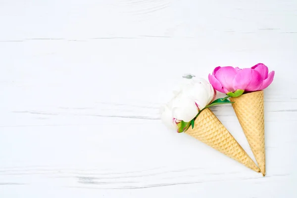 Ice cream cones with peonies flower and leaves on white wooden background. Summer concept. Copy space, top view