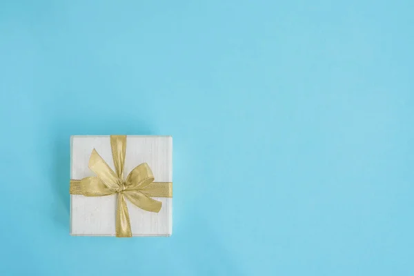 贈り物やプレゼント ボックスは 明るい青の背景に金色のリボンで飾られました 上面図 空間をコピーします グリーティング カード ミニマリズム — ストック写真