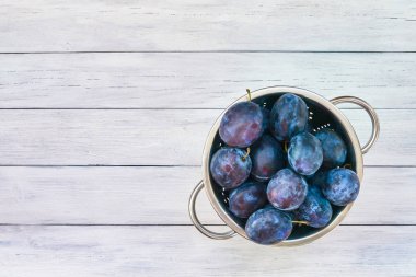 Beyaz ahşap masa üzerinde kevgir içinde mor Erik. Üstten Görünüm, kopya alanı