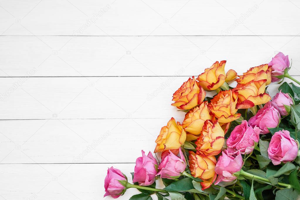 Pink and yellow roses on white wooden background. Bouquet of colorful roses. Copy space, top view. Greeting card.