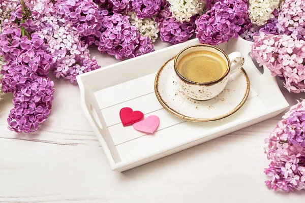 Spring lilac flowers and cup of coffee with hearts on white background. Valentines Day concept. Copy space. Greeting card
