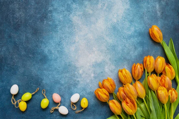 Easter background. Decorative Easter eggs and spring tulips on blue background. Copy space, top view. Flat lay of Easter celebration concept.