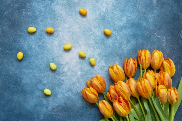 Blue Easter background. Decorative Easter eggs and spring tulips on blue background. Copy space, top view. Flat lay of Easter celebration concept.