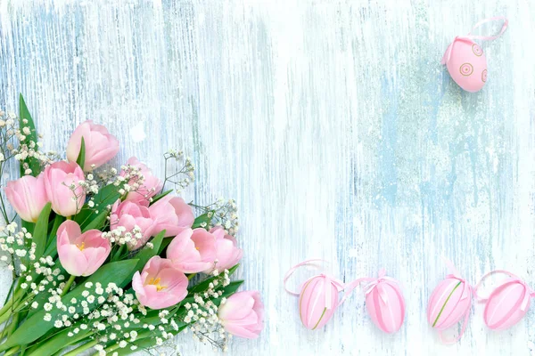 Easter background. Decorative Easter pink eggs and pink tulips on blue background. Copy space, top view. Easter celebration concept.