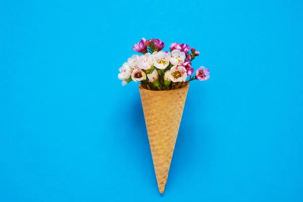 Cône de crème glacée avec de petites fleurs sur fond bleu. Espace de copie, vue du dessus . — Photo