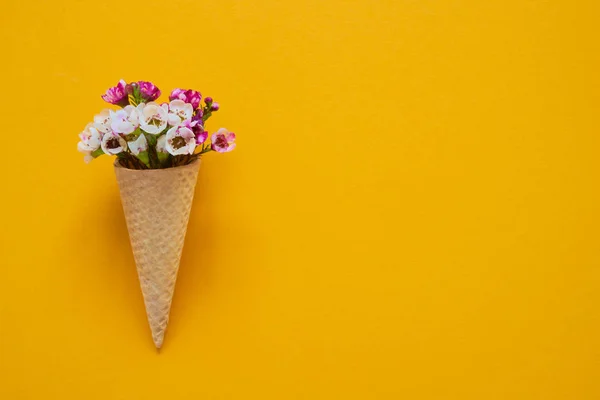 Cono de helado con flores pequeñas sobre fondo amarillo. Copiar espacio, vista superior . — Foto de Stock