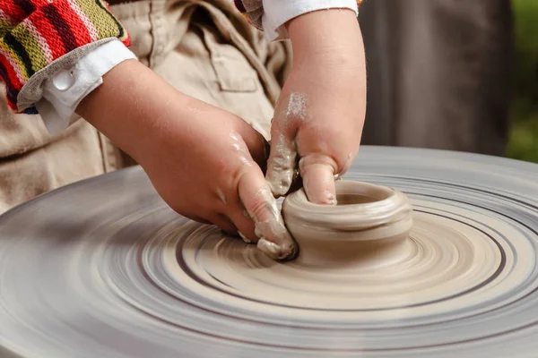Rotating potter's wheel and clay ware on it taken from above. A sculpts his hands with a clay cup on a potter's wheel. Hands in clay.