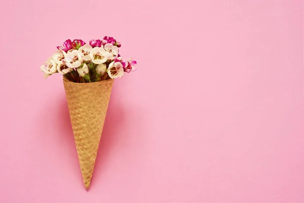 Cône de crème glacée avec de petites fleurs sur fond rose. Espace de copie — Photo
