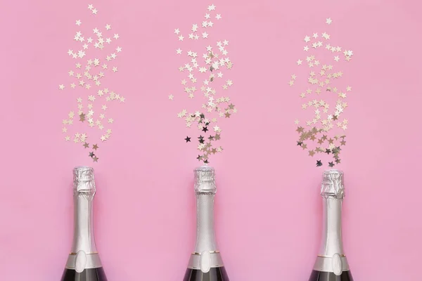 Tres botellas de champán con estrellas de confeti sobre fondo rosa . — Foto de Stock